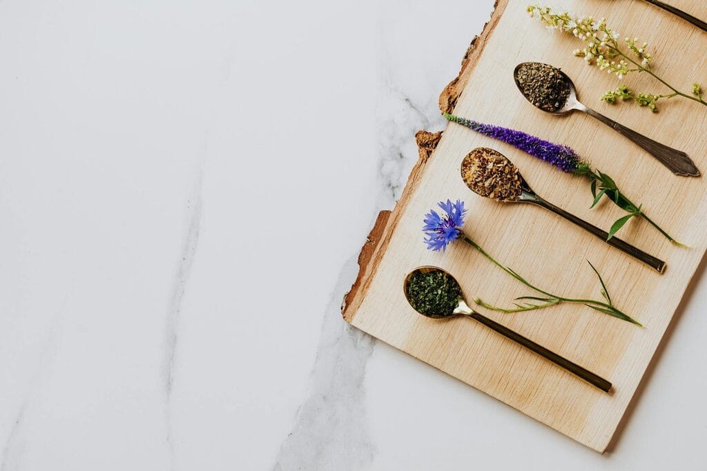 Dried herbs and wildflowers on wooden spoons on a marble surface