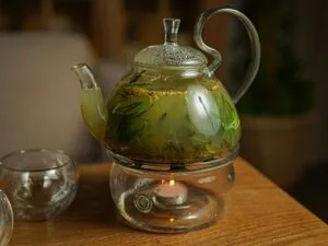 A glass teapot of herbal tea brewing on a candle warmer, evening mood