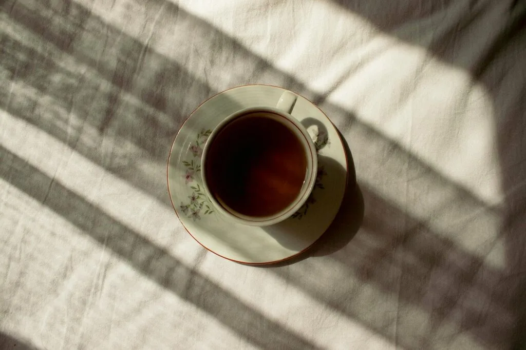 A vintage tea cup of amber loose leaf tea on linen, soft window shadows